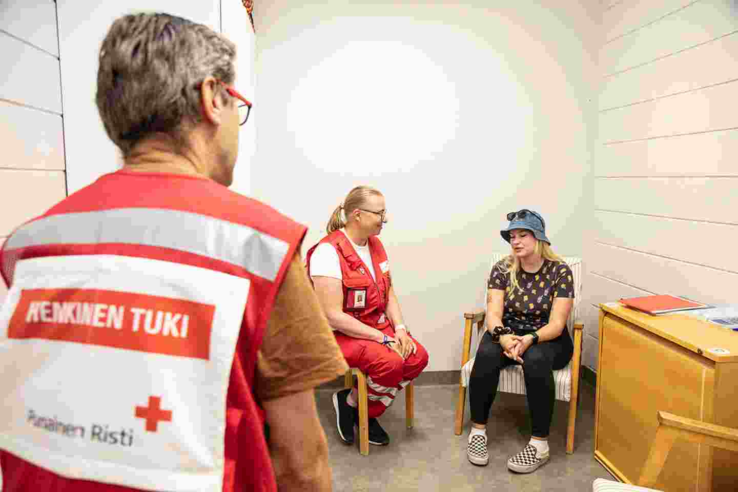 Kaksi henkilöä istuu vierekkäin keskustelemassa. Toinen on Punaisen Ristin vapaaehtoinen. Kolmas henkilö, Punaisen Ristin vapaaehtoinen, on selin kameraan päin.