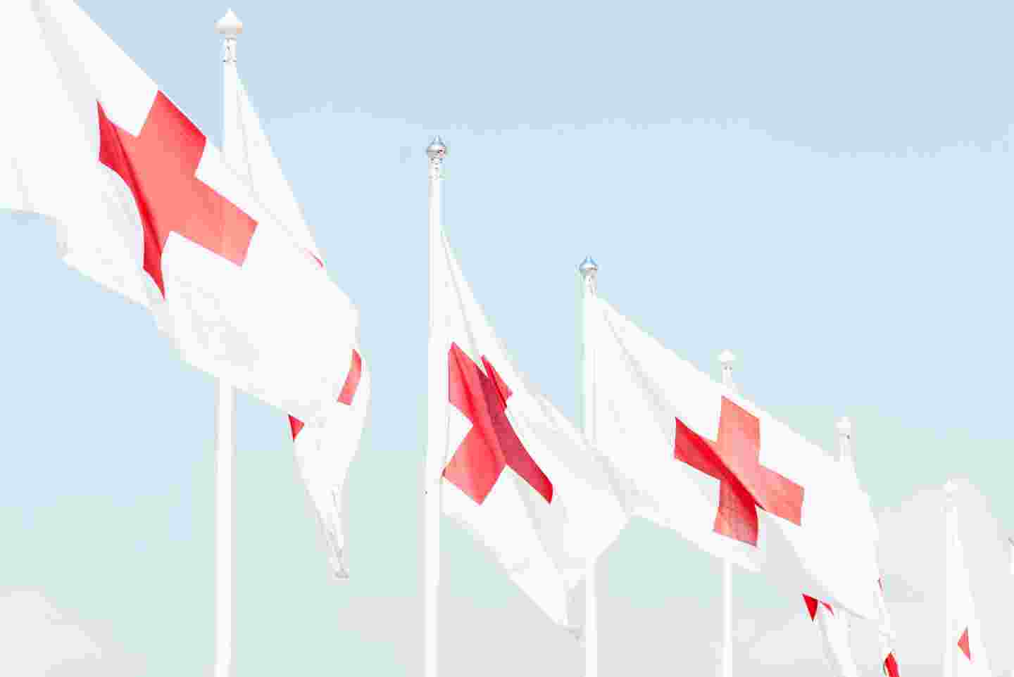 Punaisen Ristin lippuja liehumassa lipputangoissa.