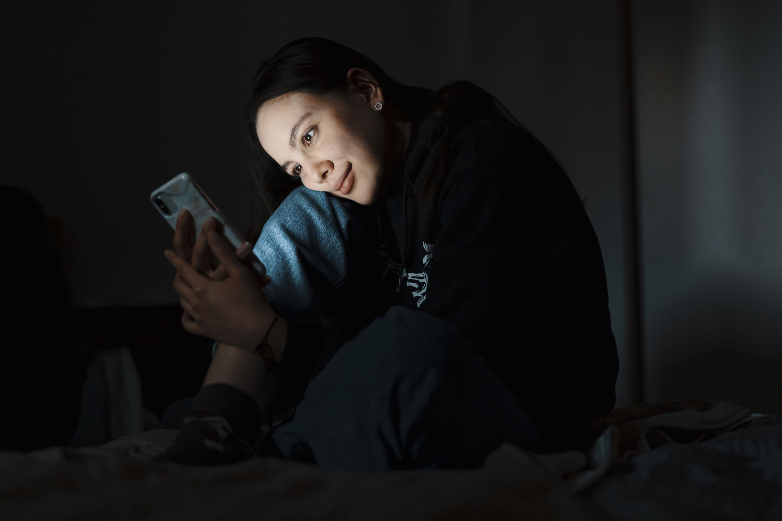 Nuori katsoo pimeässä puhelintaan ja hymyilee