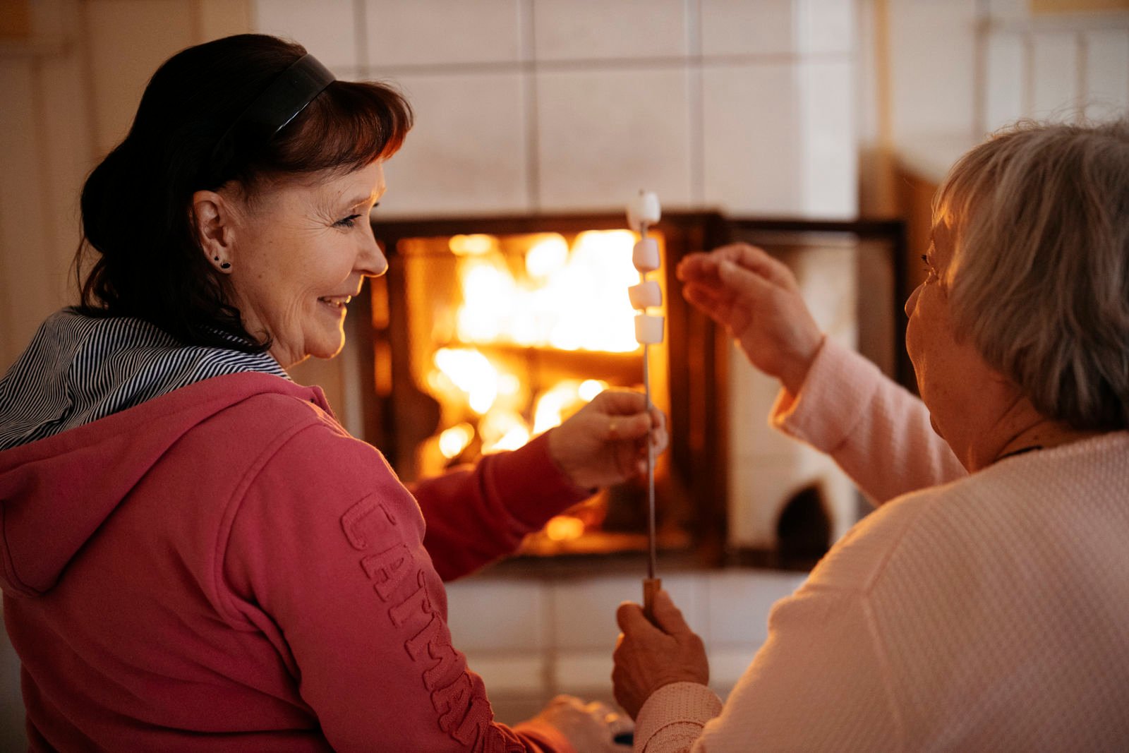 Kaksi ihmistä paahtaa vaahtokarkkeja takan ääressä.