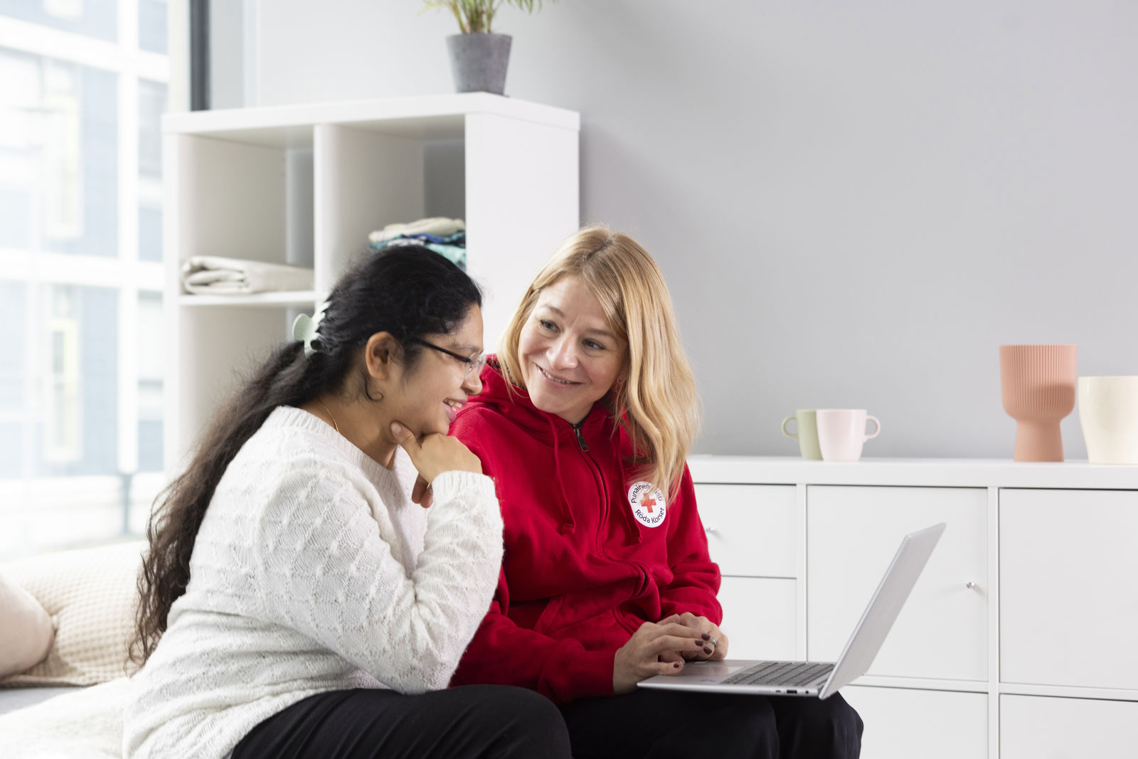 Ihmisiä pöydän ääressä. Kaksi ihmistä katsoo etuajalla kameraan hymyillen. 