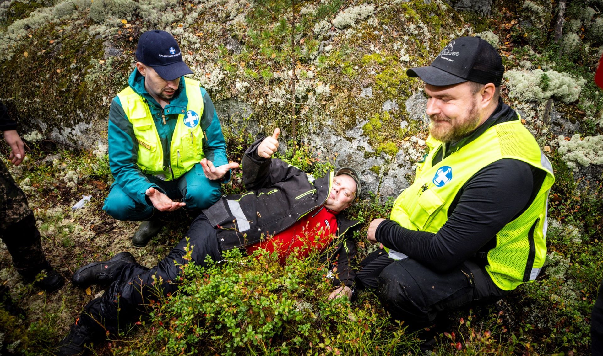 Ihmisiä metsässä. Yksi näyttelee loukkaantunutta, mutta näyttää paukkua.