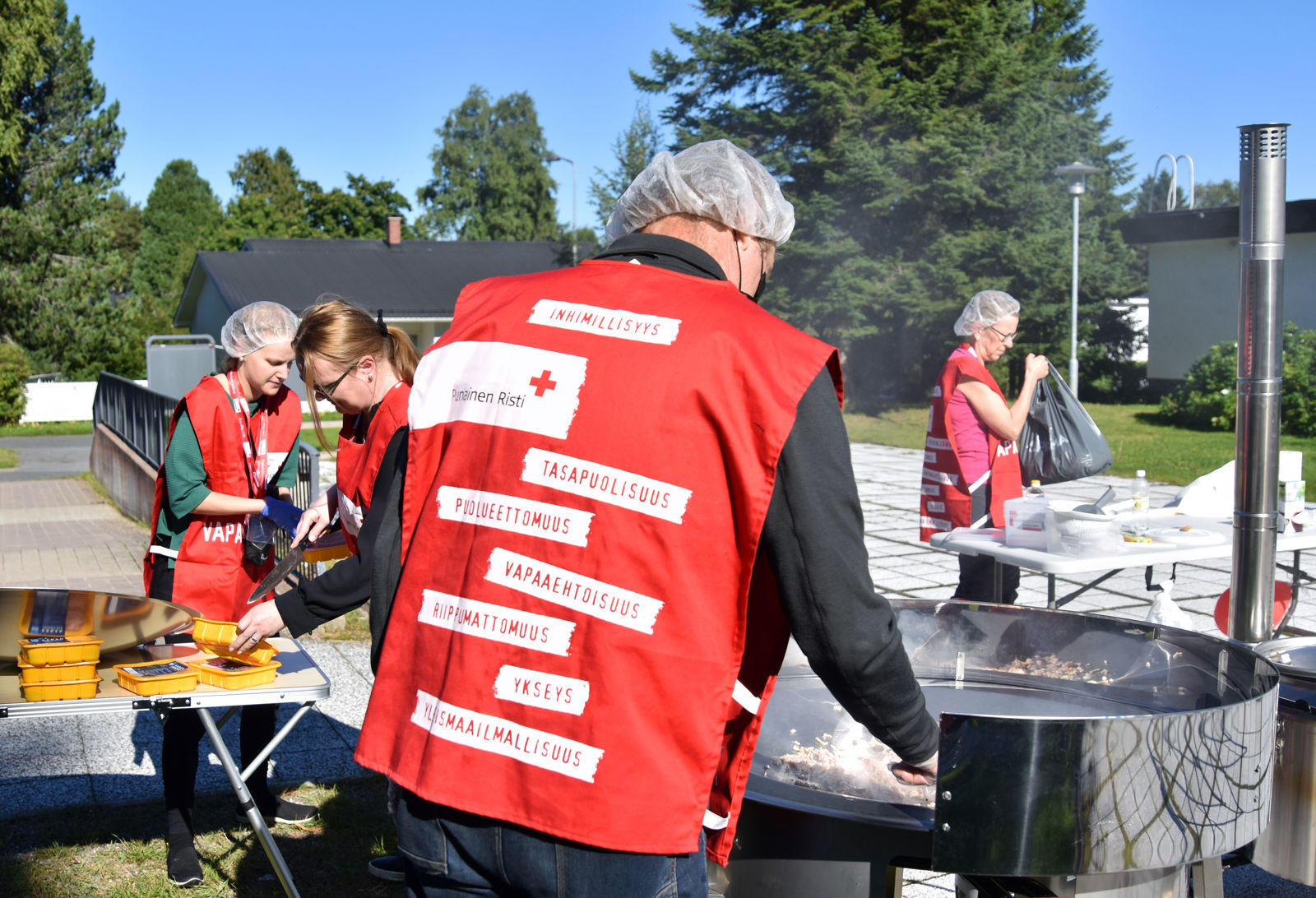 Punaisen Ristin liivit päällä oleva ruoka-avun vapaaehtoinen tekee ruokaa.