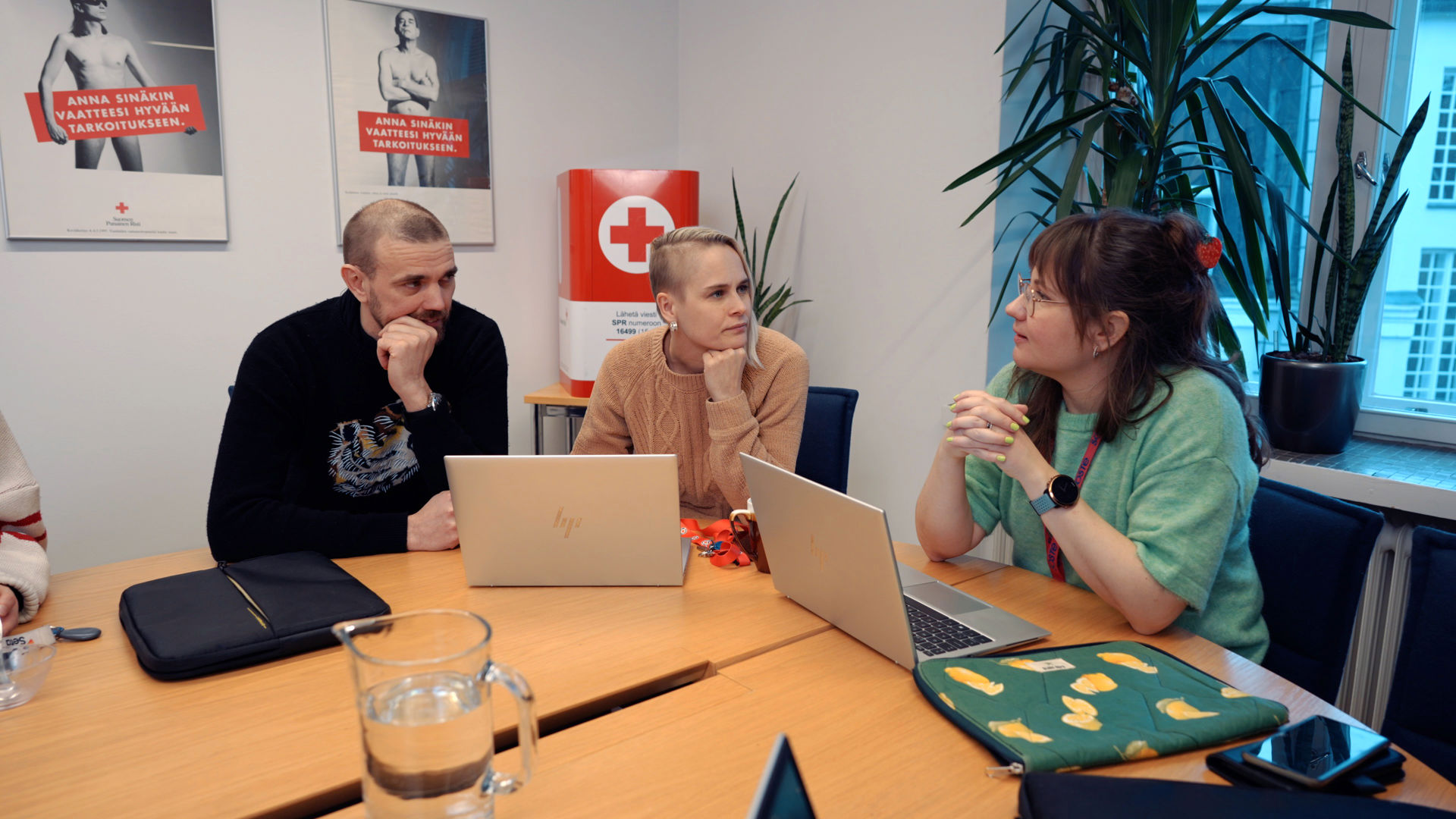 Kolme henkilöä kannettavien tietokoneiden kanssa pöydän ääressä.