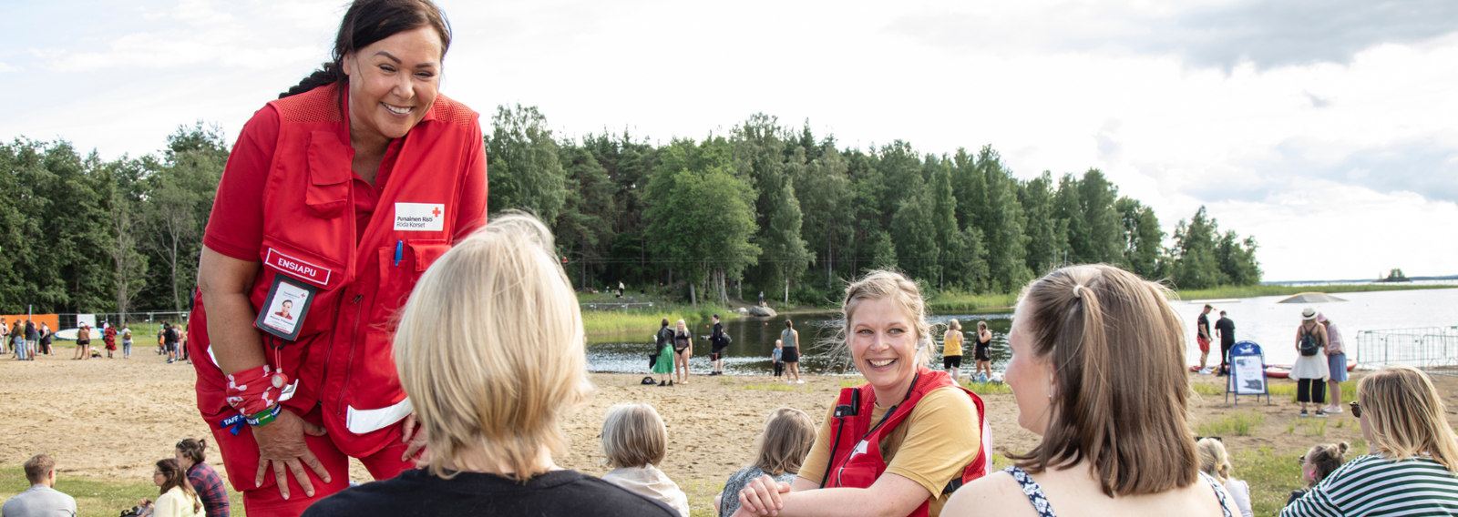 Punaisen Ristin vapaaehtoinen juttelee festarivieraille hiekkarannalla.