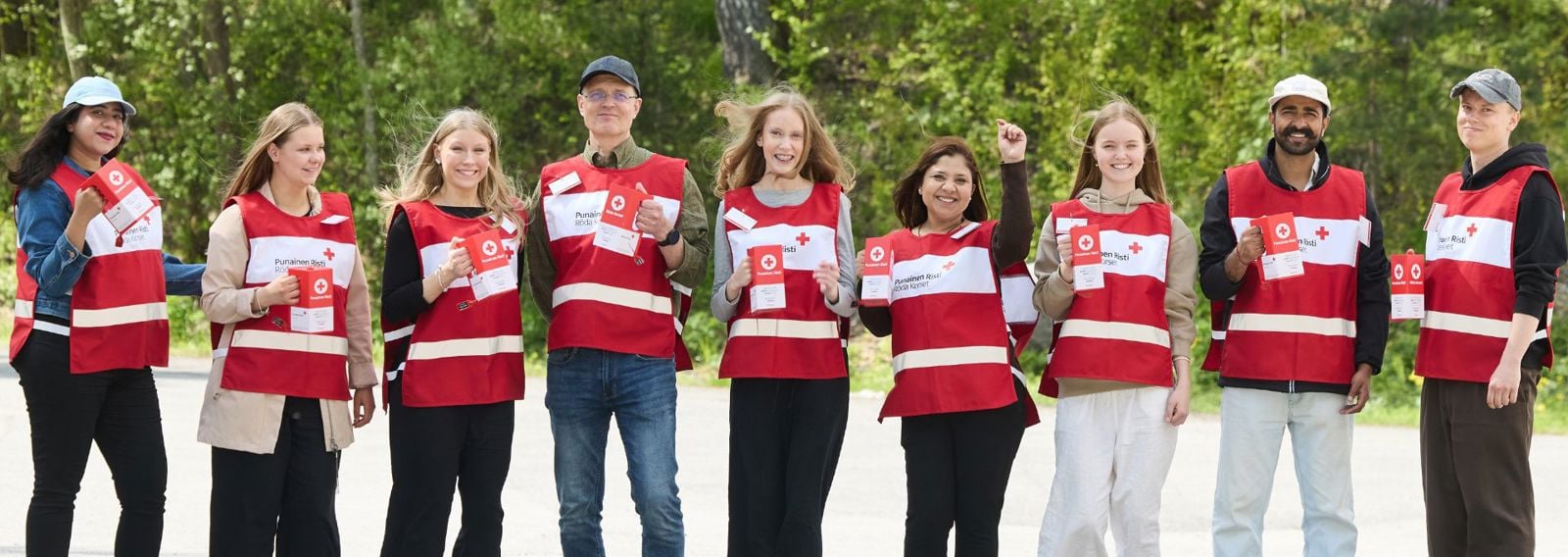 Kaksi ihmistä poseeraa Punaisen Ristin liiveissä keräyslippaiden kanssa