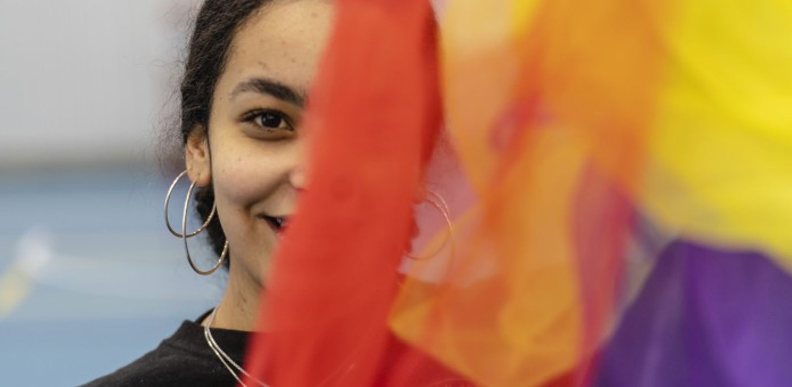 Ihminen katsoo hymyillen kameraan värikkään kankaan takaa.