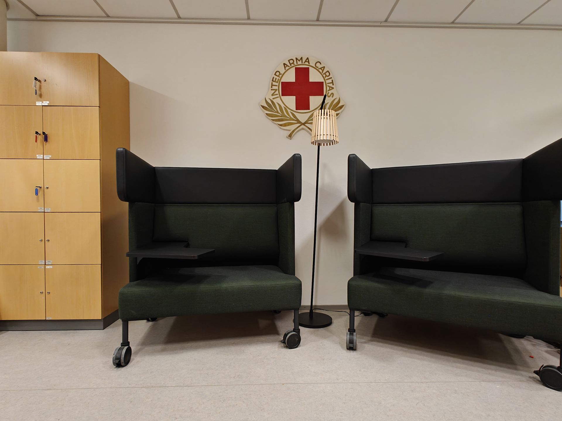 Kaksi työskentelynojatuolia ja seinällä taulu, jossa Punaisen Ristin motto "Inter Arma Caritas".