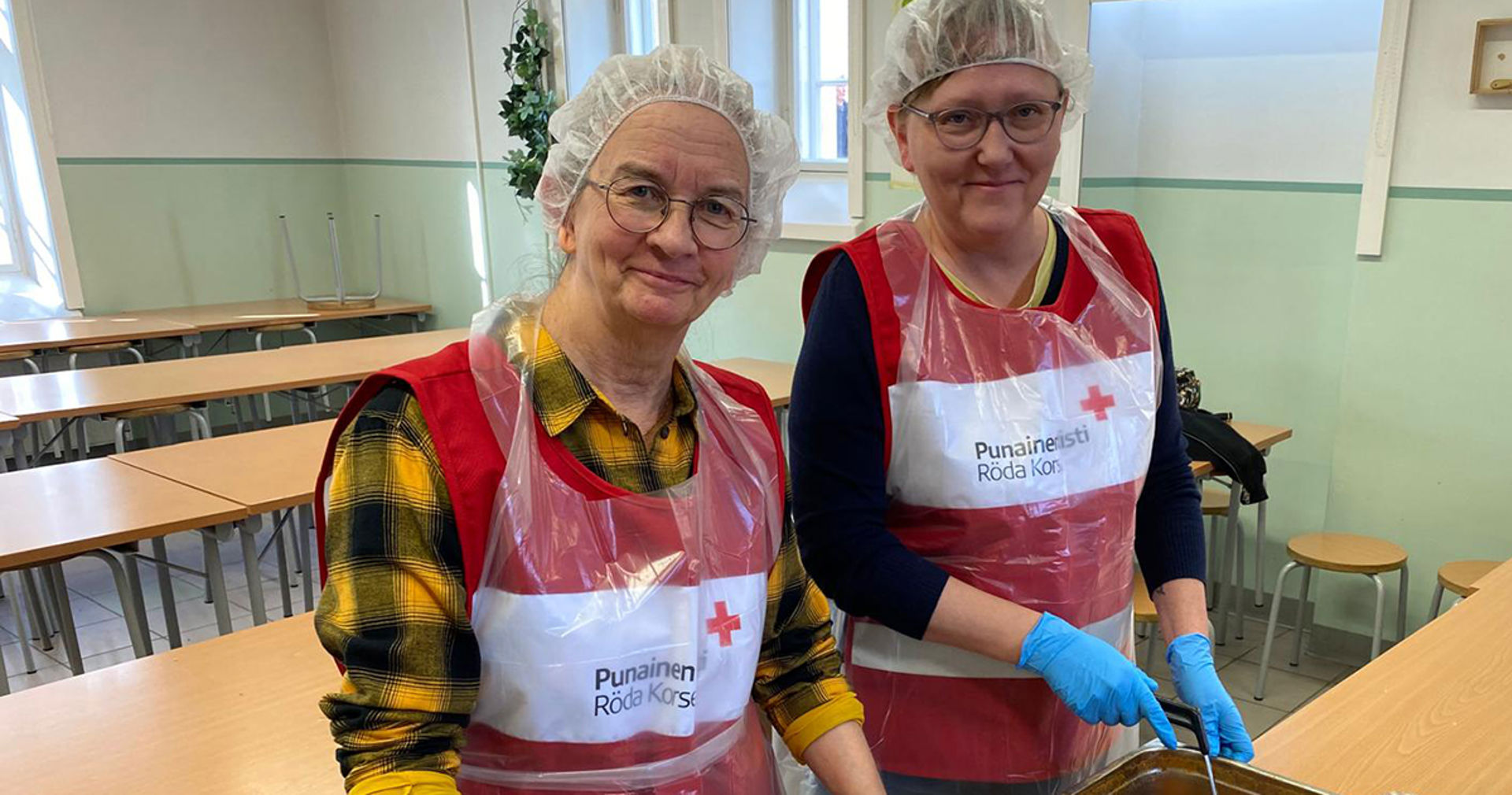 Kaksi hymyilevää Punaisen Ristin vapaaehtoista jakamassa koulun ylijäämäruokaa.