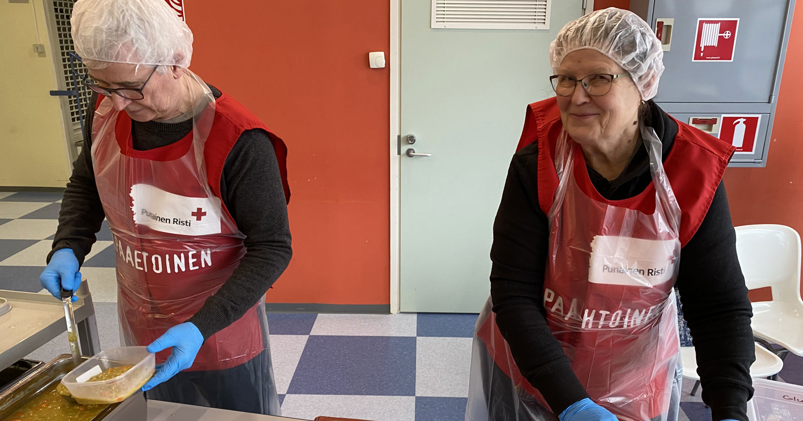 Ihminen annostelemassa ruokaa astiaan Punaisen Ristin liivi päällään