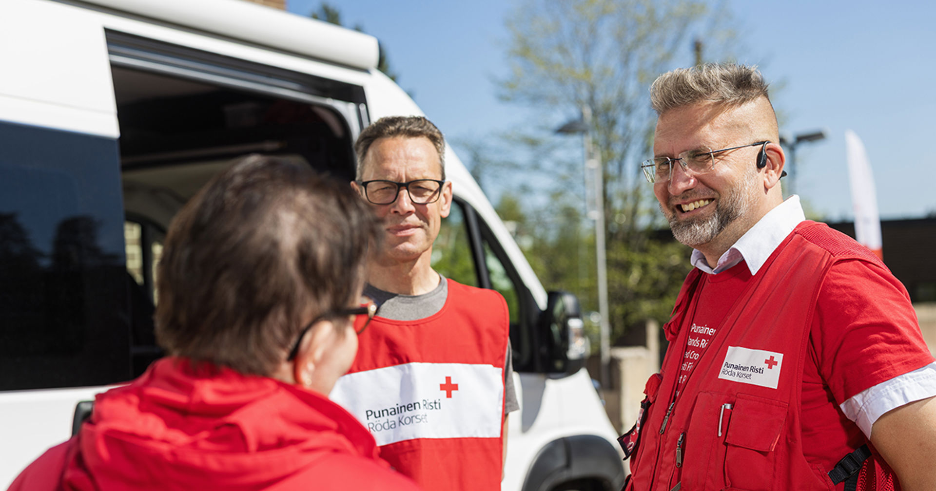 Kaksi hymyilevää henkilö ulkona juttelemassa kolmannen henkilön kanssa. 
