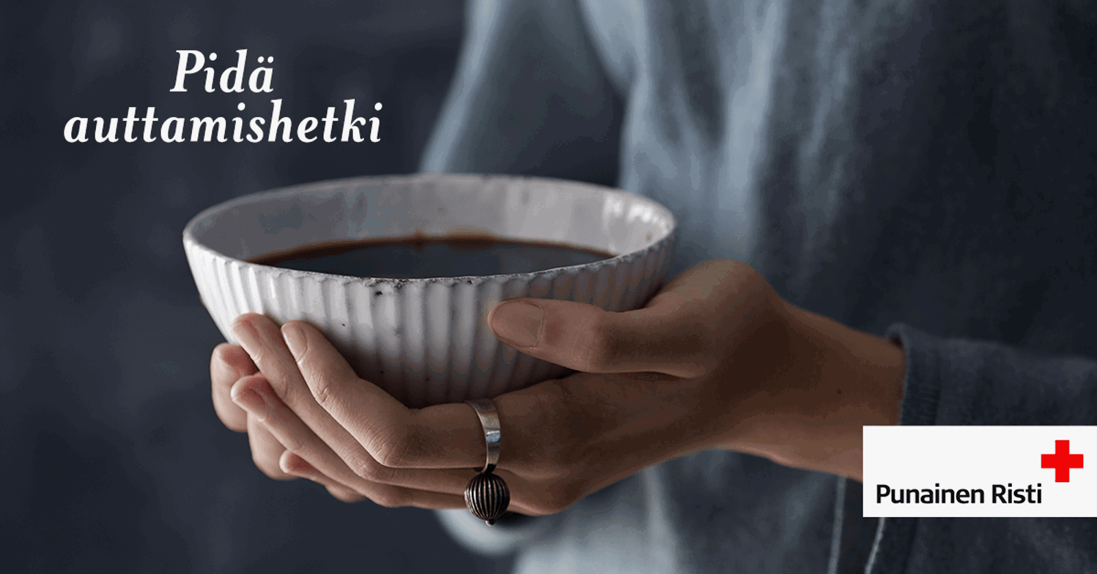 Kädet, jotka kannattelevat isoa kahvikuppia, Teksti Pidä Auttamishetki sekä Punaisen Ristin logo.