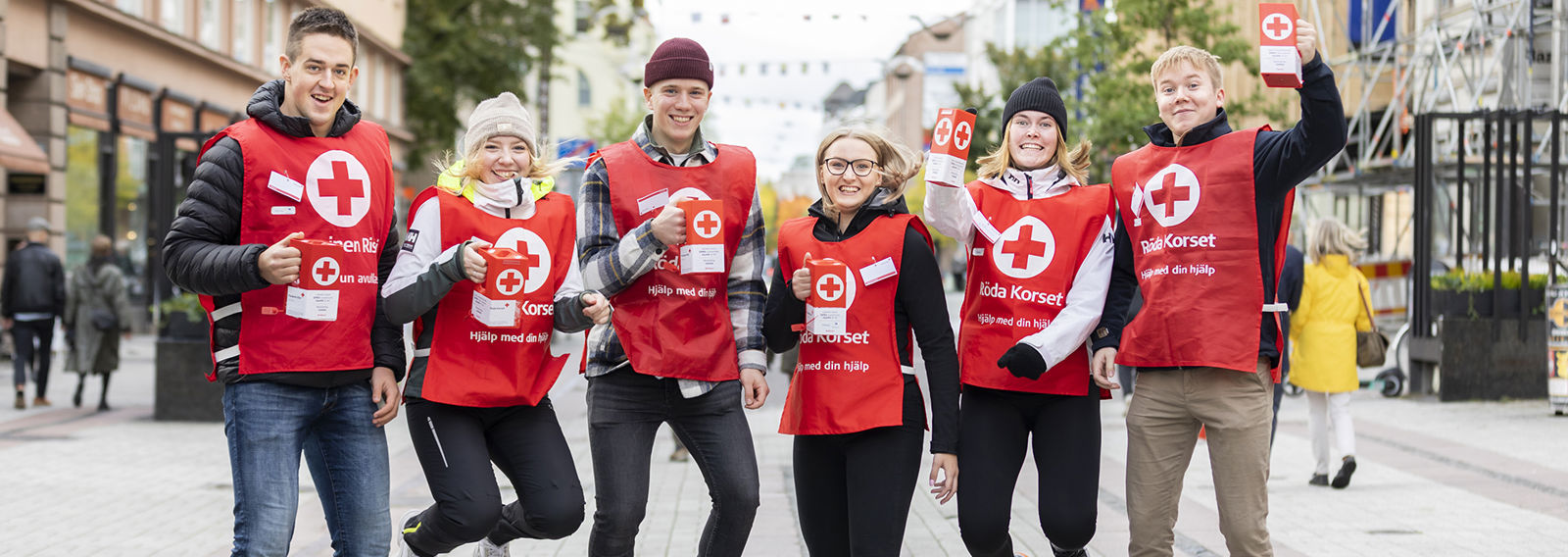 Kuusi nuorta punaliivistä vapaaehtoista, ja heillä on keräyslippaat kädessään.