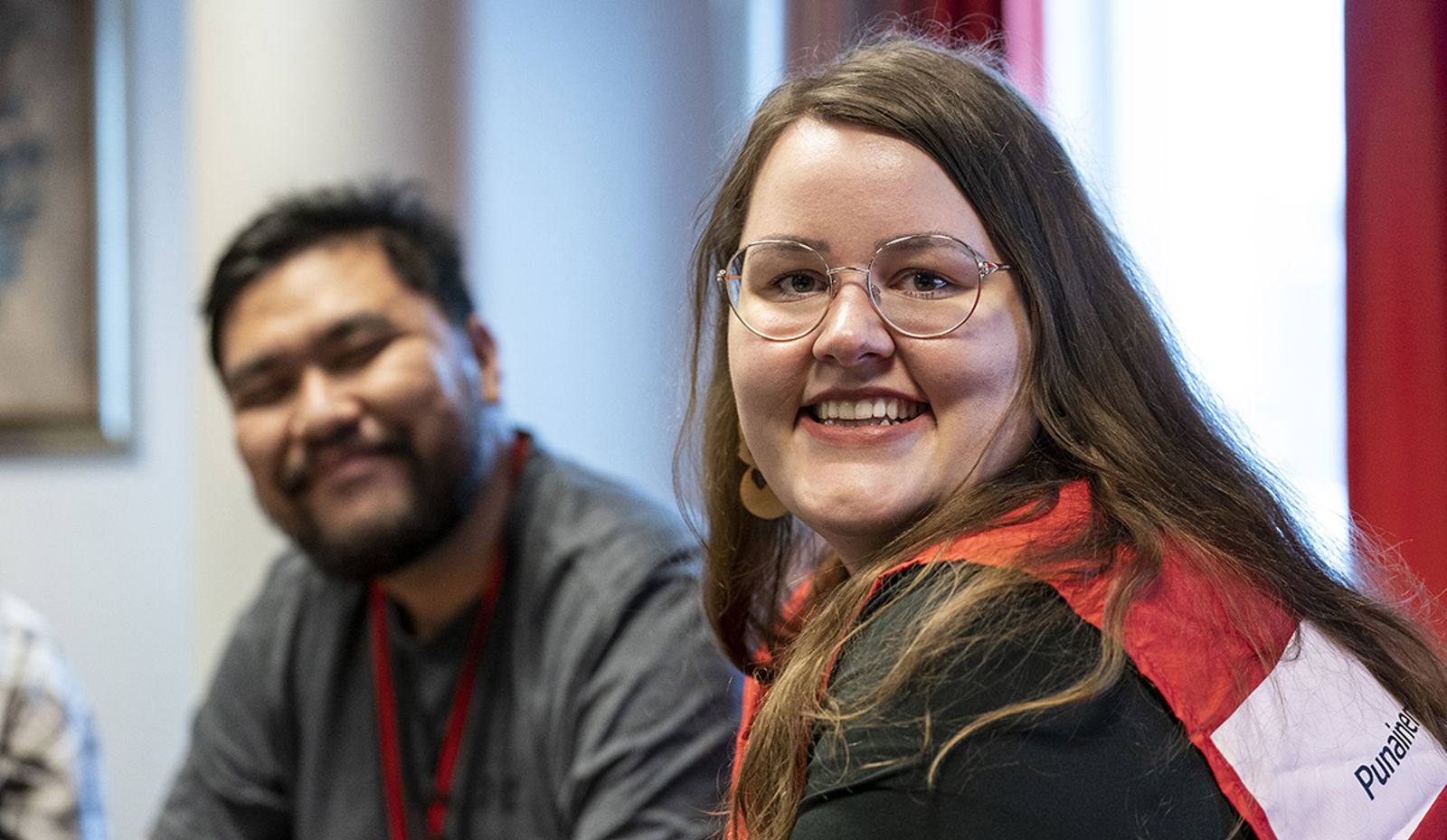 Kaksi hymyilevää henkilöä istuu kasvot kohti kameraa.